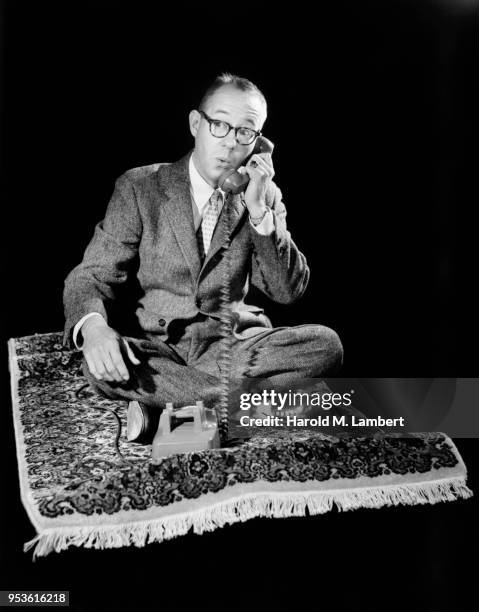 MID ADULT MAN SITTING ON MAGIC CARPET AND TALKING ON TELEPHONE