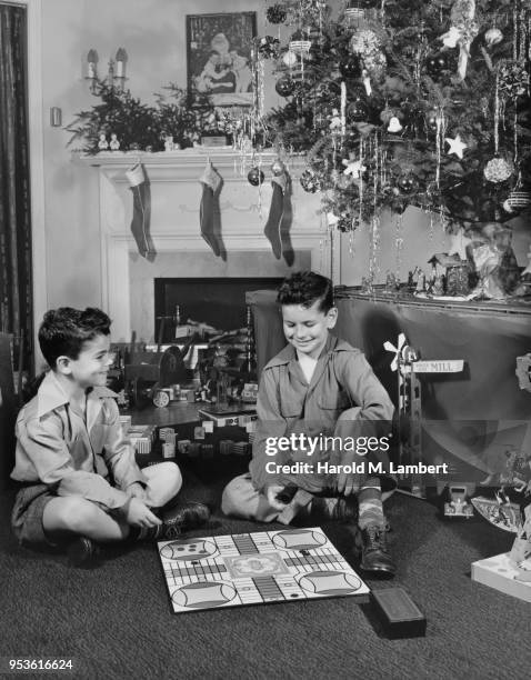 BOYS PLAYING BOARD GAME IN FRONT OF CHRISTMAS TREE