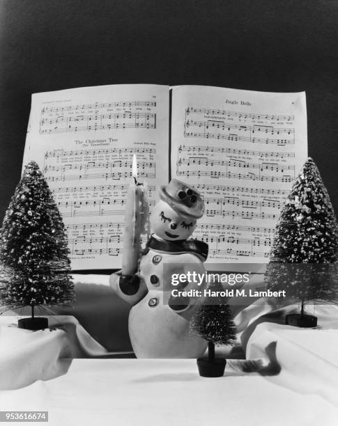 SNOWMAN FIGURINE AND CHRISTMAS DECORATIONS WITH SHEET MUSIC IN BACKGROUND