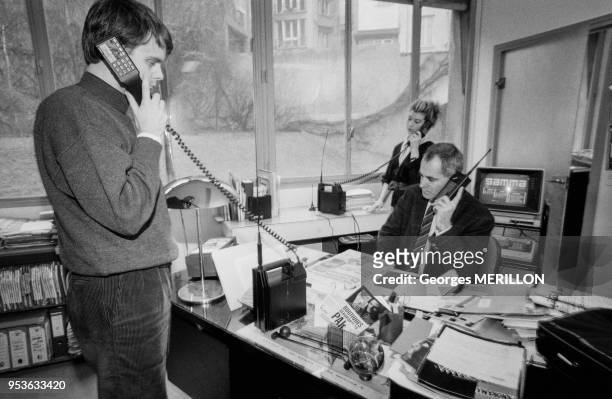 Le directeur de la rédaction Floris de Bonneville assis à son bureau et à gauche Bernard Derenne, éditeur, utilisant le plus petit téléphone portatif...