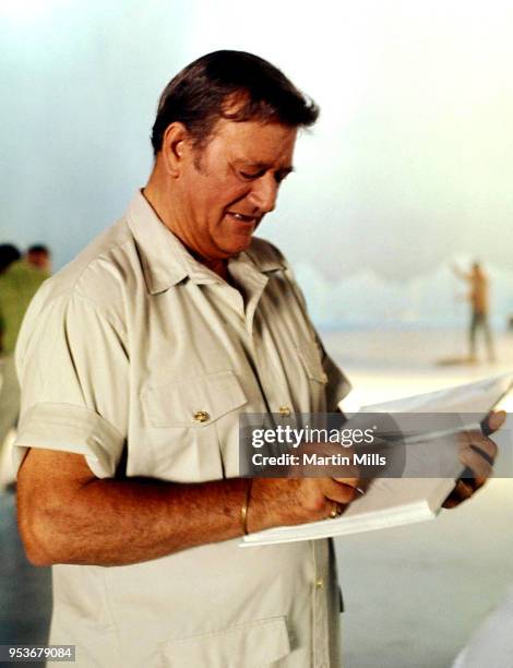 American actor and filmmaker John Wayne autographs a book circa 1960's.