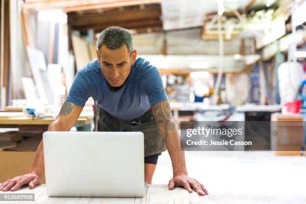 a builder/carpenter works on his computer in his workshop - new zealand small business stock pictures, royalty-free photos & images