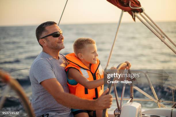 little boy sitting with father and steering with sailboat - father son sailing stock pictures, royalty-free photos & images