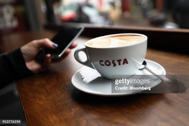 Cup of coffee sits nest to a customer as they browse their smartphone in a Costa Coffee shop, operated by Whitbread Plc, in London, U.K., on...