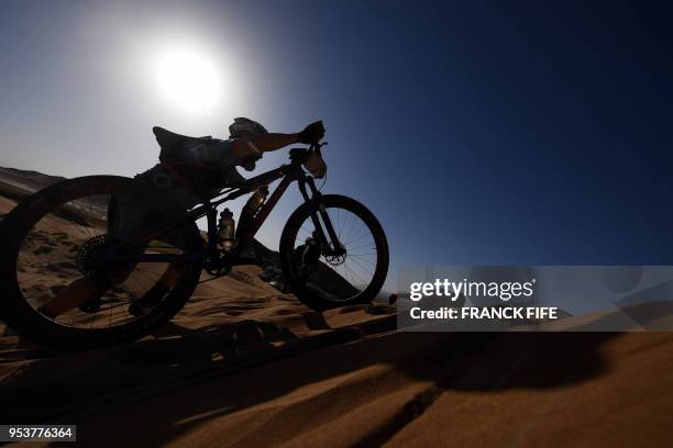 Competitors push their bikes up a sand dune during Stage 4 of the 13th edition of the Titan Desert 2018 mountain biking race between Boumalne Dades...