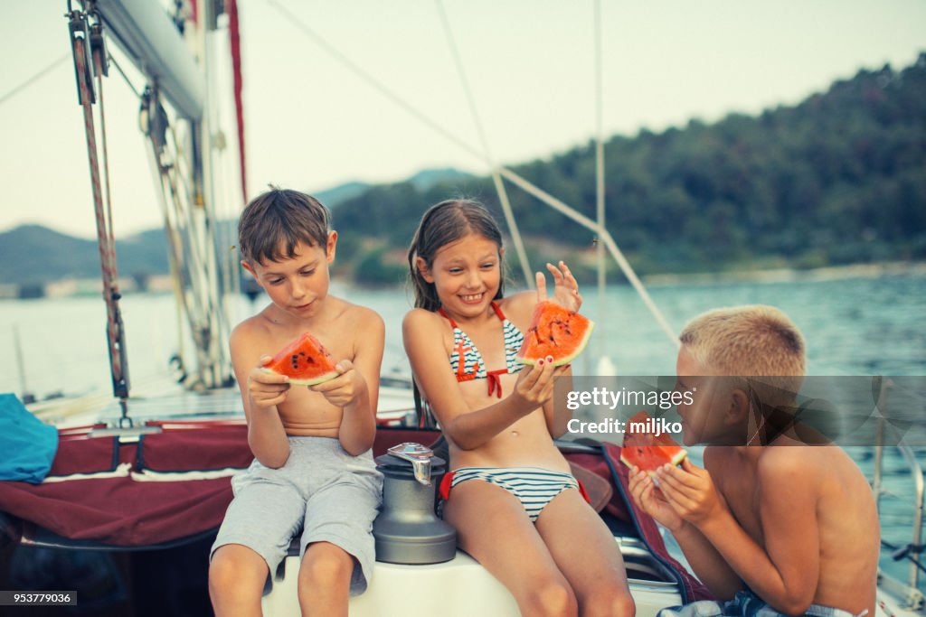 ヨットの上で新鮮なスイカを食べている子供たち
