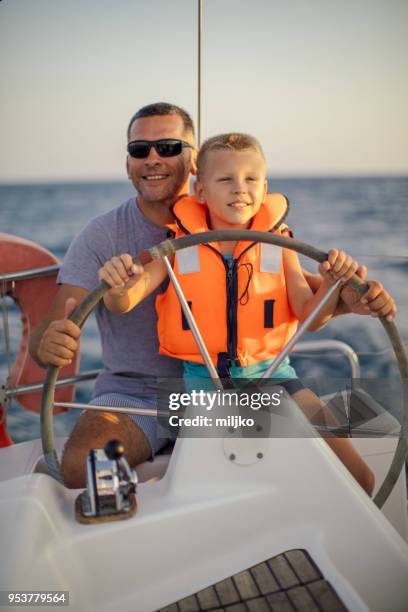 little boy sitting with father and steering with sailboat - father son sailing stock pictures, royalty-free photos & images