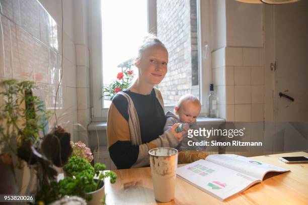 portrait of mother and baby son sitting in kitchen at home - babyhood photos et images de collection