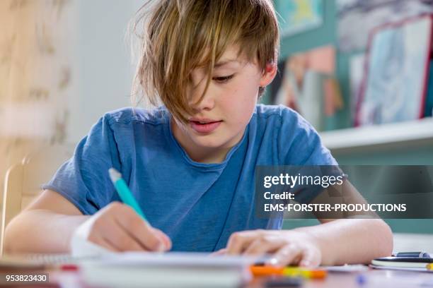 10 years old blonde school boy while doing his homework. - 10 11 years boy stock pictures, royalty-free photos & images