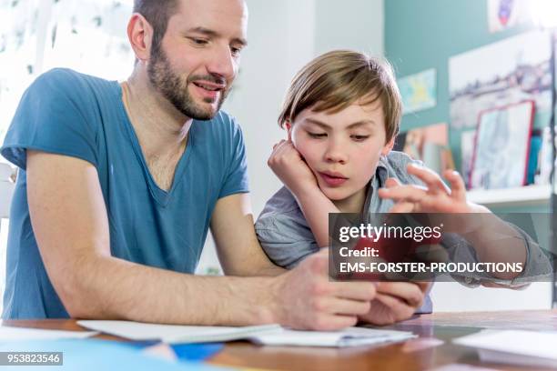 private tutoring lesson for 10 years old blonde elementary school boy while doing his homework together with male tutor in his thirties. - 35 39 years stockfoto's en -beelden