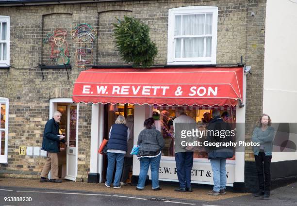 People queue outside E W Revett and Son butcher shop, Wickham Market, Suffolk, England, UK.