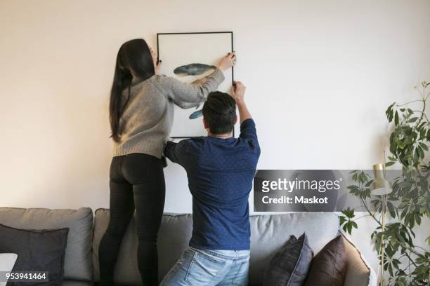 couple hanging painting while leaning on sofa at home - house for an art lover stock pictures, royalty-free photos & images