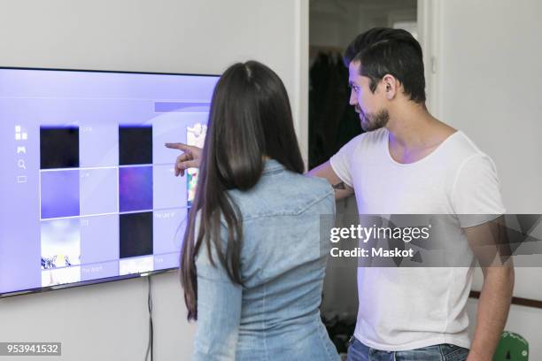 young couple using touch screen television mounted on wall in living room - smart tv living room stock pictures, royalty-free photos & images