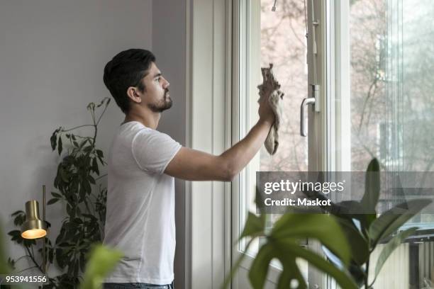 side view of young man cleaning glass window in living room - cleaning equipment stock pictures, royalty-free photos & images