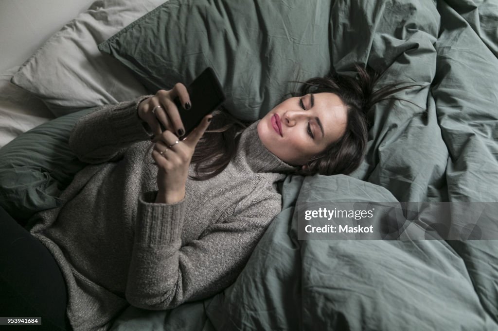 High angle view of woman using smart phone while lying on bed