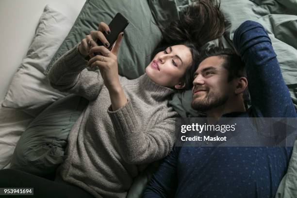 high angle view of smiling couple taking selfie through smart phone while lying on bed - smart communicate elevation view stockfoto's en -beelden