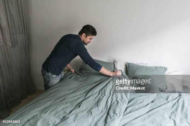 high angle view of man making bed while standing in bedroom at home - bett machen stock-fotos und bilder