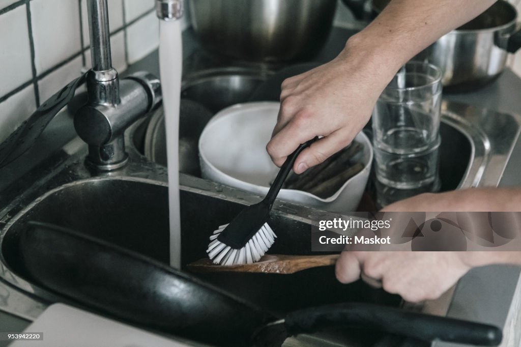 Cropped image of man washing wooden spoon with dish brush in sink at kitchen