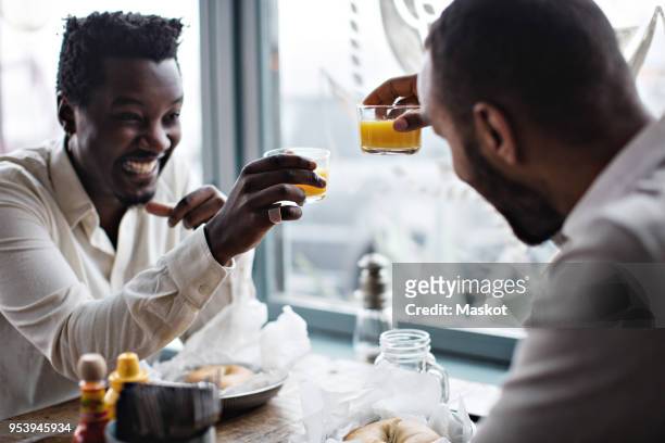 happy friends toasting drinks while sitting at table in restaurant - male friendship stock pictures, royalty-free photos & images