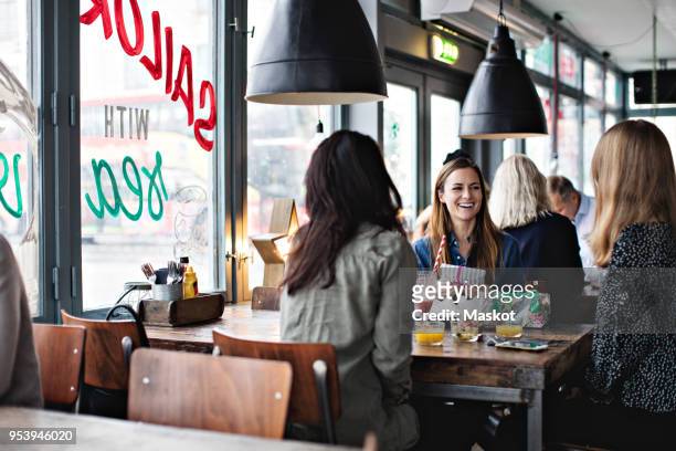 smiling female friends enjoying while sitting at dining table for brunch in restaurant - brunch stock-fotos und bilder