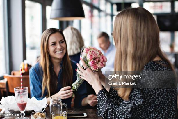 smiling young woman giving fresh flower bouquet to female friend sitting at restaurant - flower presents bildbanksfoton och bilder