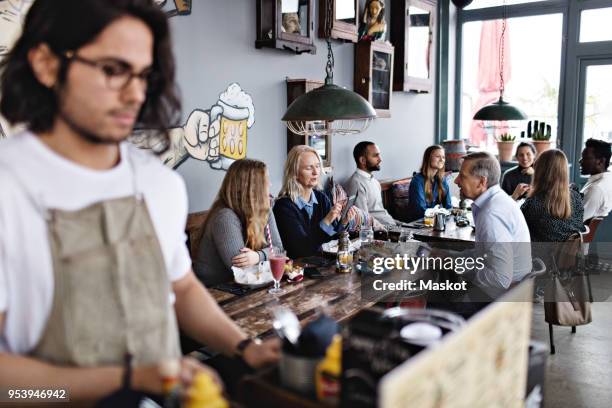 customers having brunch while young male owner standing in lectern - family with one child mother bonding family adult daughter focus on background leisure stock-fotos und bilder