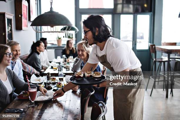 waiter serving food to smiling customers at restaurant - kellnerberuf stock-fotos und bilder