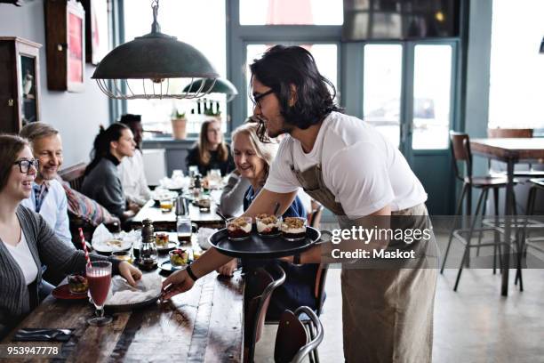 waiter serving food to smiling customers at restaurant - servir à manger et à boire photos et images de collection