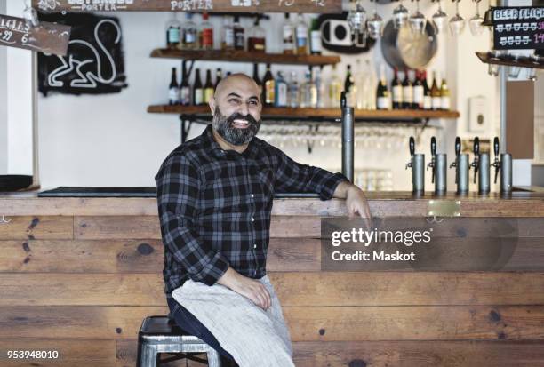 confident smiling bartender sitting by bar counter - local bar photos et images de collection