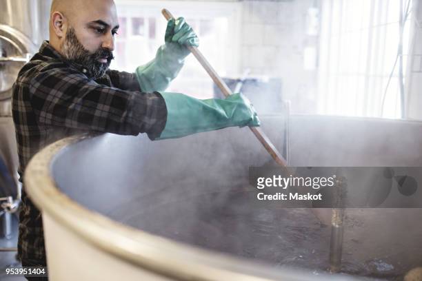 mid adult worker stirring beer in container while working at brewery - beer ingredients bildbanksfoton och bilder