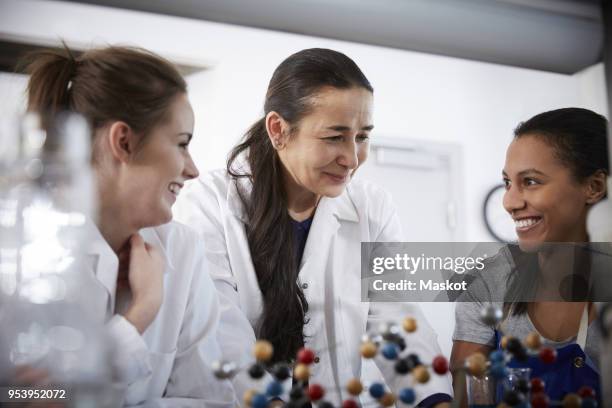 smiling mature chemistry teacher with young female students in classroom at university - scientist standing next to table stock-fotos und bilder