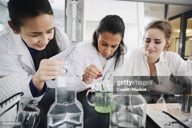 mature chemistry teacher looking at young university student mixing liquid solution in beaker - liquid solution stock pictures, royalty-free photos & images