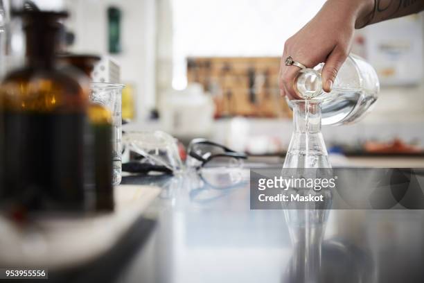 cropped hand of female student pouring liquid solution in flask from bottle at laboratory - liquid solution stock pictures, royalty-free photos & images