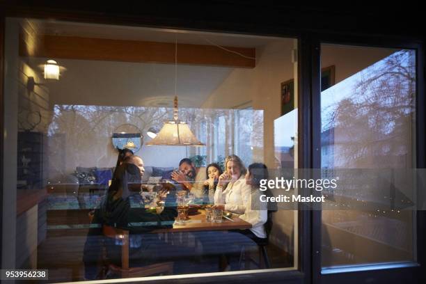 happy family having dinner at table seen through glass window during sunset - family home exterior stock-fotos und bilder