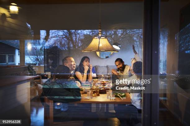 multi-generation family talking while having dinner at table seen through window - evening meal stock-fotos und bilder