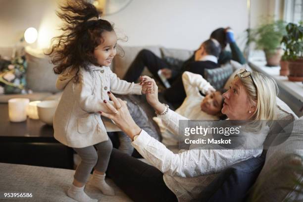 Girl playing with grandmother on sofa by family at home