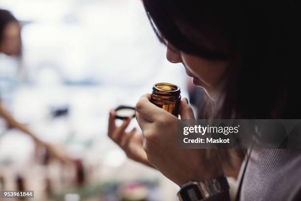 young woman smelling perfume from bottle at workshop - smell stockfoto's en -beelden