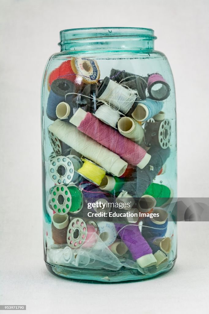 Glass jar of small thread rolls and bobbins