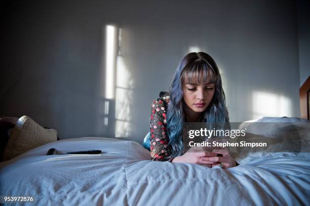 teen with long hair looks at phone on bed - looking at camera foto e immagini stock