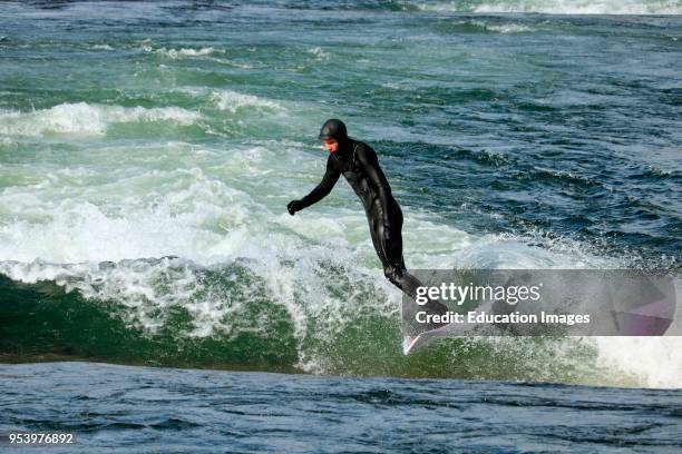 Wet suit clad surfer rides whitewater wave in a water park along the Deschutes River in Bend Oregon.