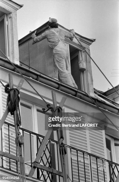 Un ouvrier du batiment restaure une fenêtre du 6ème étage d'un immeuble sans système de sécurité, Paris, septembre 1979, France.