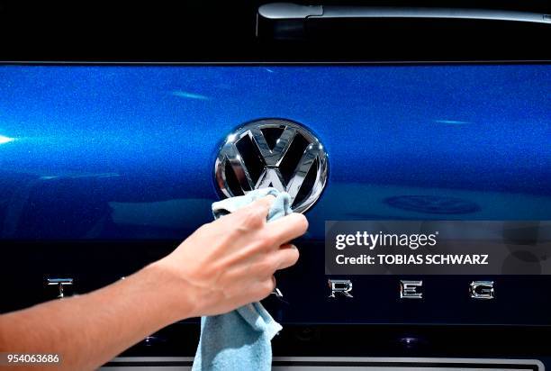 Staff member cleans the rear logo of an SUV VW Touareg on display ahead of the annual general meeting of German carmaker Volkswagen, in Berlin on May...
