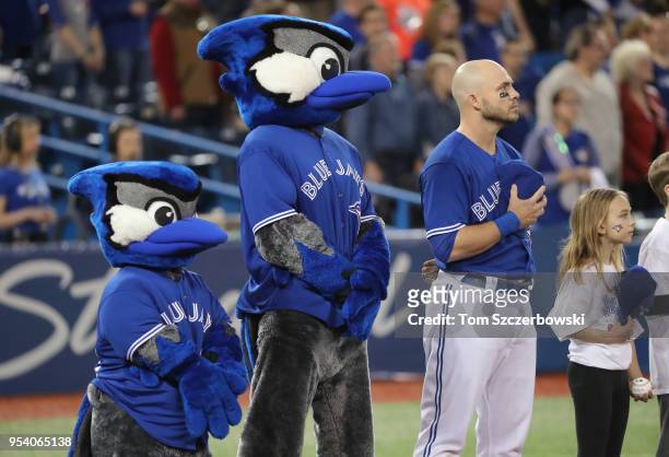 Steve Pearce of the Toronto Blue Jays stands for the playing of the national anthems alongside mascots Ace and Junior before the start of their MLB...