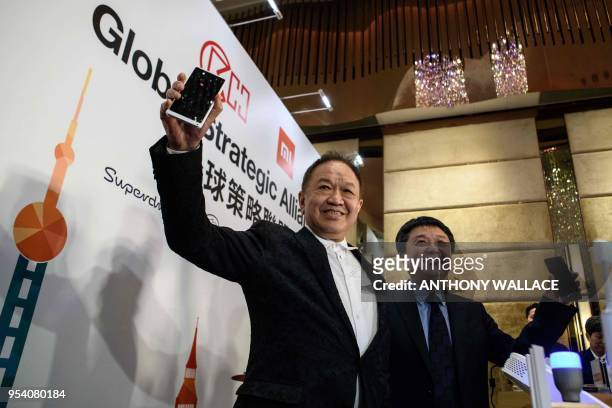 Canning Fok , group co-managing director for CK Hutchison , and Xiang Wang , senior vice president for Xiaomi, pose with mobile phones during a joint...