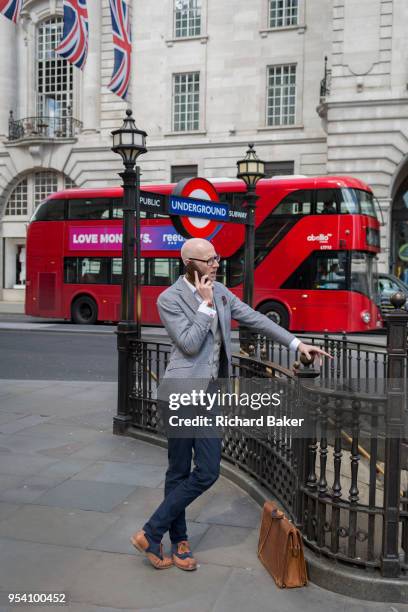 Well-dressed young man talks on his phone while leaning on railings at a Piccadilly Circus underground station entrance on 1st May, in London,...