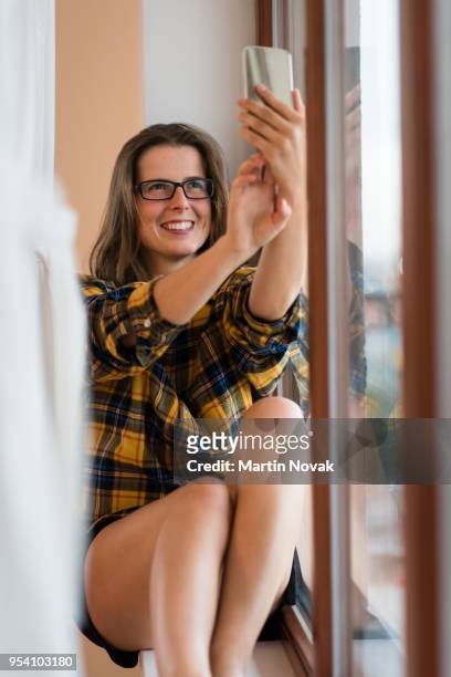 smiling woman clicking self-portrait near window - common aims stock-fotos und bilder
