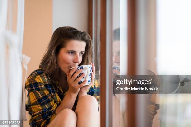 woman sipping tea while sitting near window - common aims stock-fotos und bilder