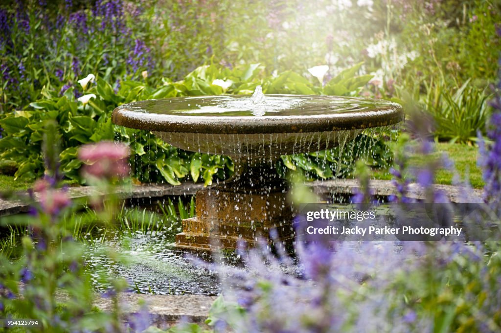 Beautiful summer garden with water fountain in amongst the flowers, in the hazy sunshine