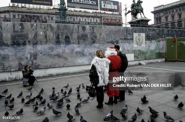 Des touristes se font photographier en compagnie du Père Noël et de pigeons sur une place en réfection à Milan, Italie.