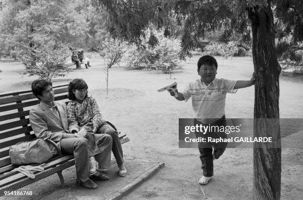 Un jeune garçon joue avec un pistolet sous l'oeil de ses parents dans un parc à Pékin le 5 juin 1988, Chine.